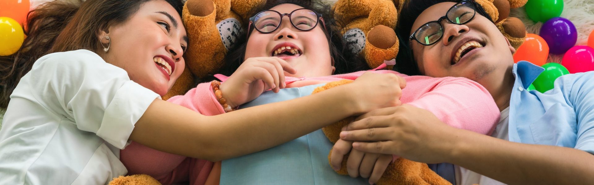Asian down syndrome teenage girl smiling and happy while spending time lying on floor in living room together with mother and father at home