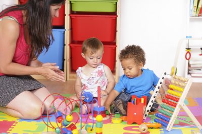 A biracial baby boyl/ toddler and his peer enjoying playtime under the spervision of their carer.